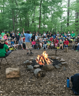 A group of kids gathered around a camp leader who is speaking